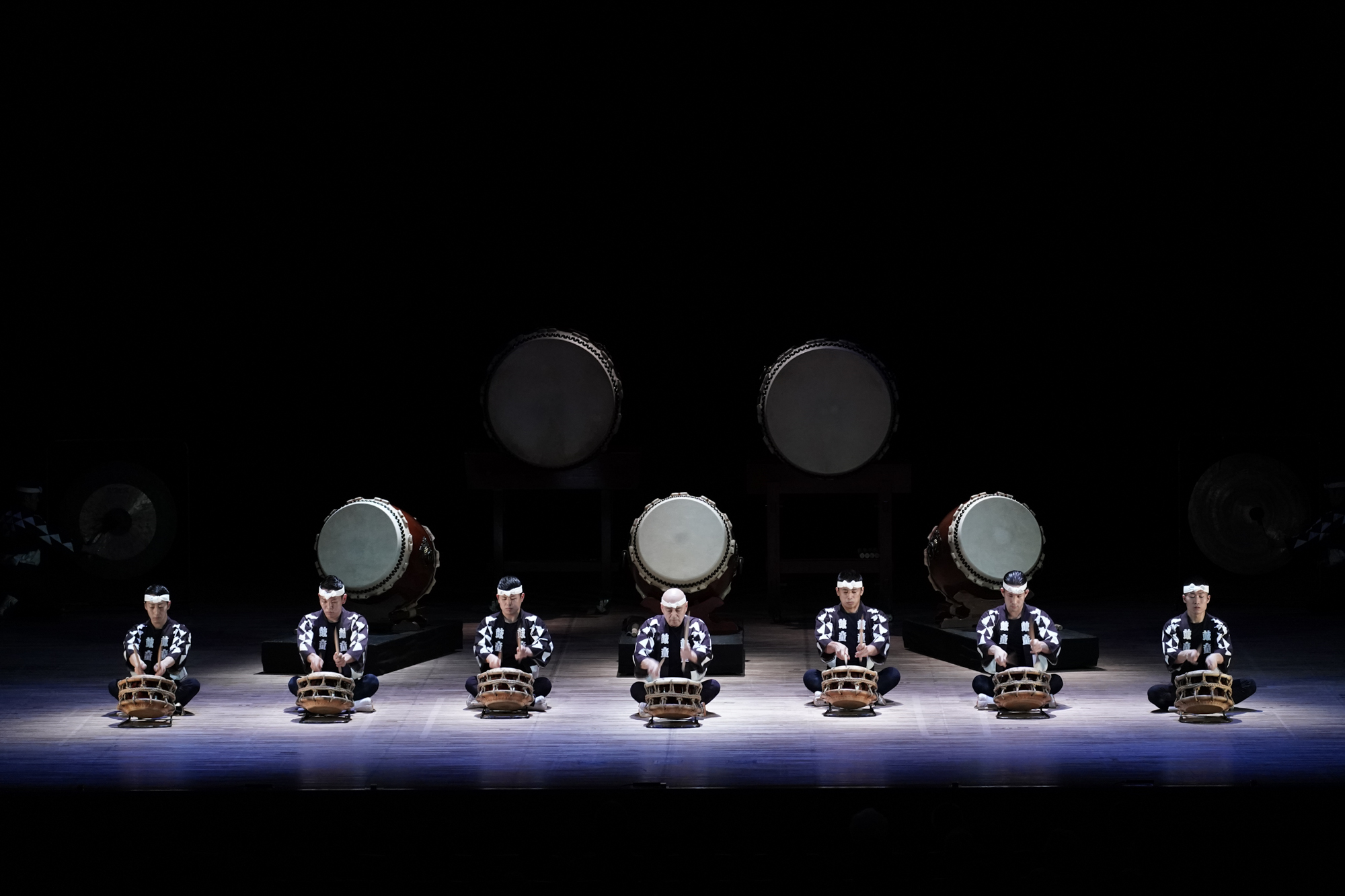 Several drummers on a darkened stage