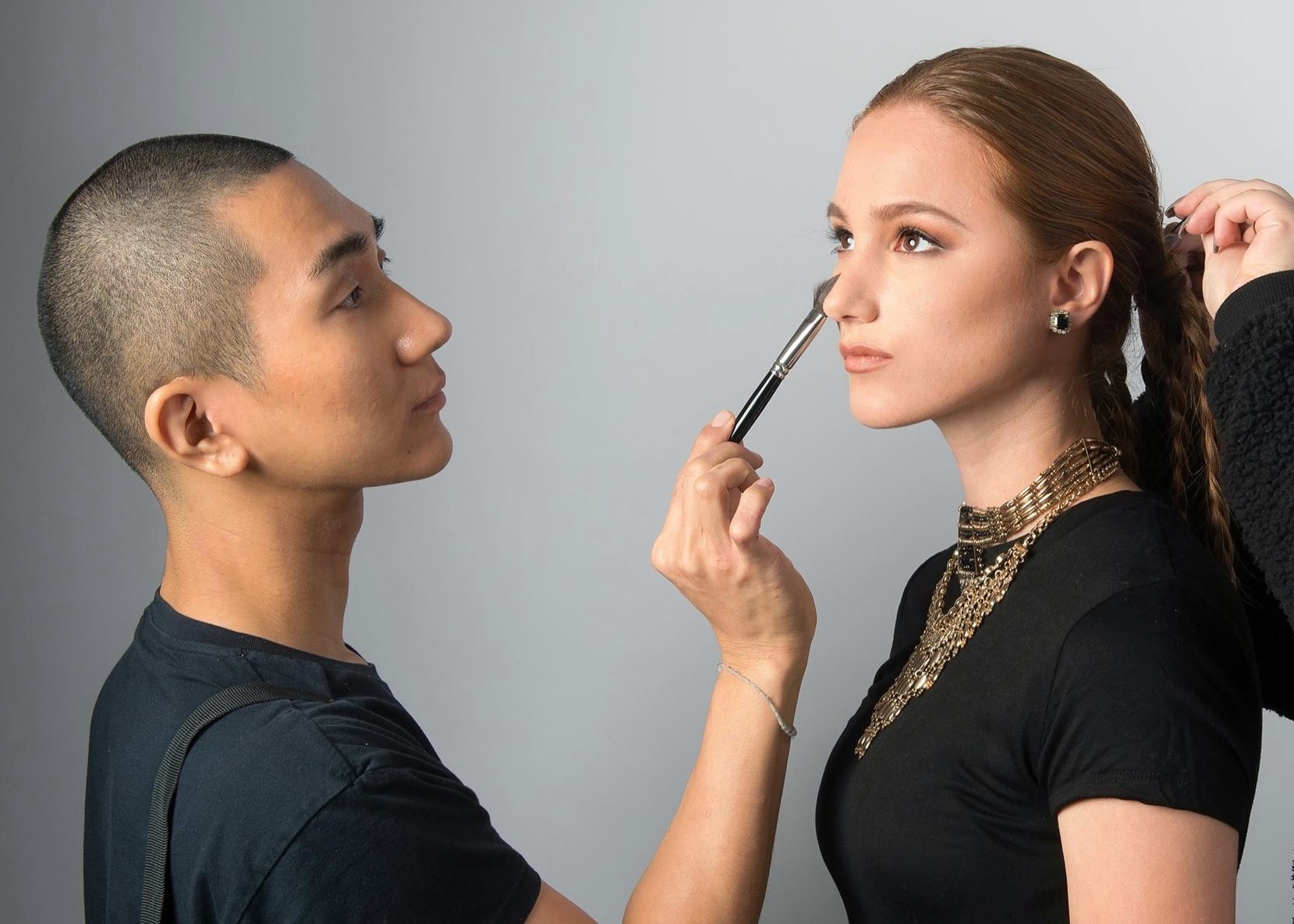 Img:Man applying make-up to the face of a female model with a brush