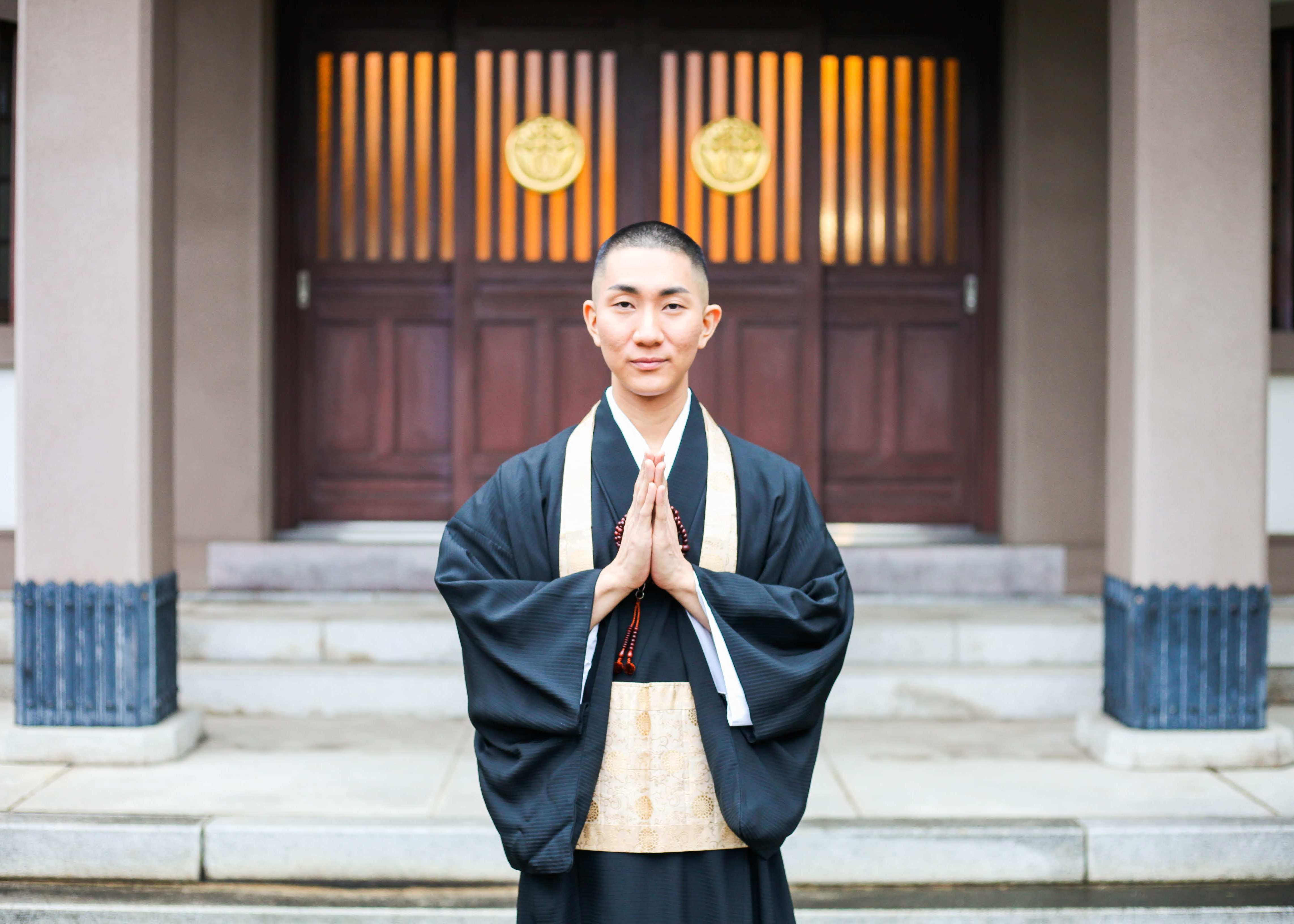 Img:Buddhist monk stand with hands together in front of a temple