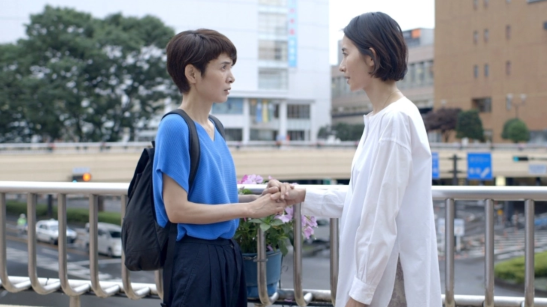 Two women standing at a railing near a Japanese train station
