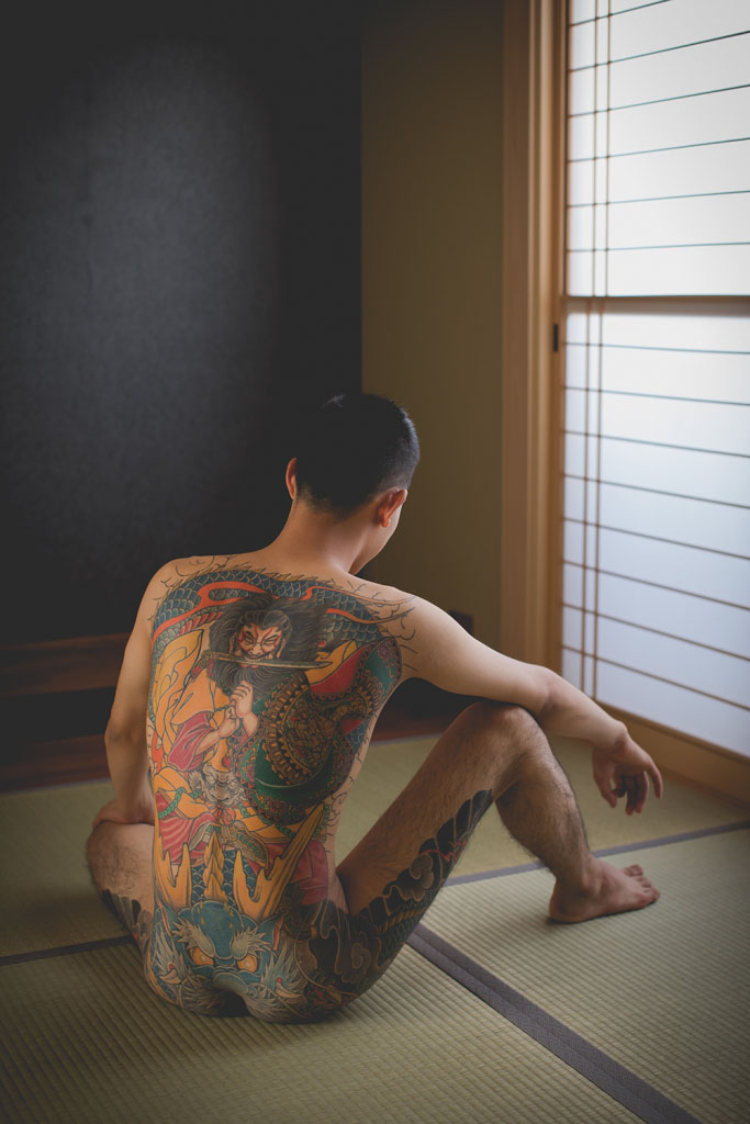 Img:Young guy sitting on Tatami showing tatoo on his back and legs