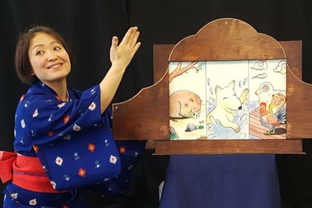 Woman in kimono gesturing to a wooden board featuring pictures
